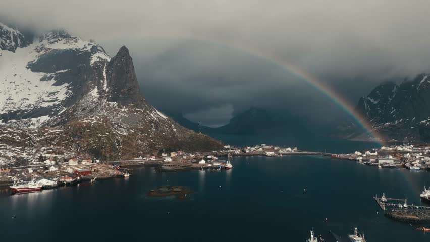 Rainbow Behind Lofoten Peaks In Reine Village, Moskenes Municipality In Nordland County, Norway. Aerial Shot