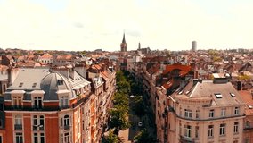 Gorgeous aerial drone footage flying in between old historic Belgium Brussels medieval houses and apartments over a neighbourhood street where green trees are towars a large church in the background. - Powered by Shutterstock - Get 15% off with code: PIKWIZARD15