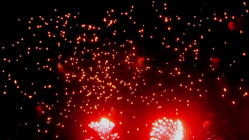 Witness an enchanting display as vibrant red fireworks burst into slow motion, illuminating the night sky during a thrilling celebration. Experience the beauty of each sparkling explosion.