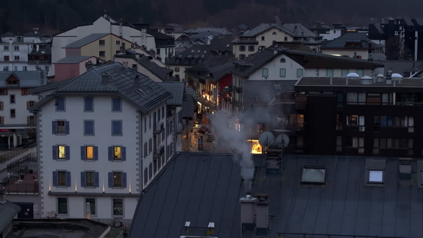 Billowing white smoke drifting from rooftop chimneys, highlighting serene evening across alpine mountain village of Chamonix near Mont Blanc