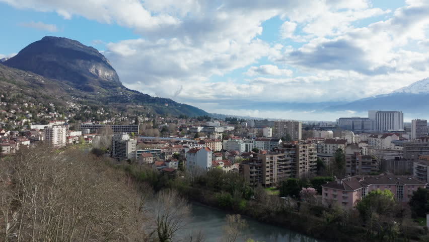 Aerial view of Grenoble city center, showcasing the Isere river winding through buildings and the Alps mountain in the background