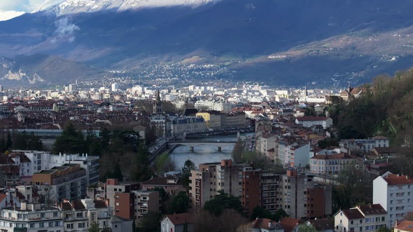 Grenoble urban landscape showcasing Isere river and its bridges, surrounding Alps under a clear blue sky during springtime