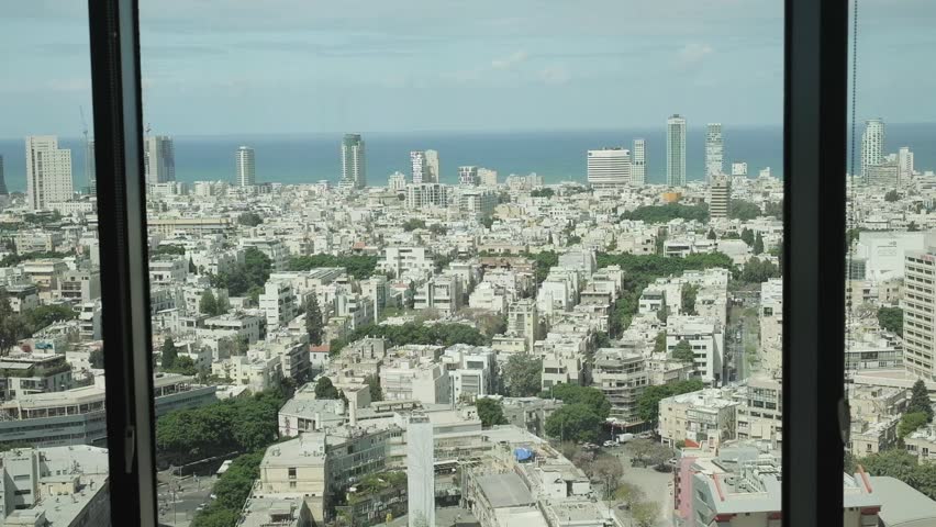 A modern city view from a window of a high building at midday, where you could see the ocean and some mid size high rises and hotels, next to older 3 to 5 stories buildings. Tel Aviv, Israel.