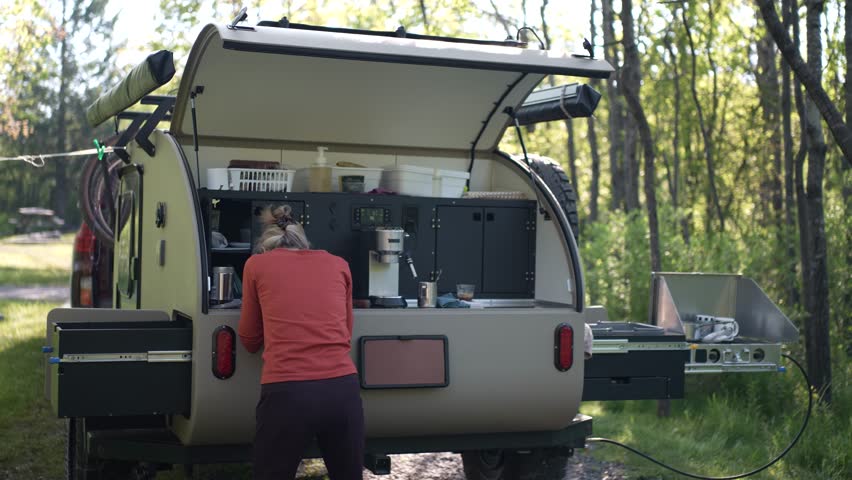 A woman is washing her face outside her camper trailer, embracing a refreshing morning in a scenic forest filled with green trees, enjoying a healthy lifestyle.