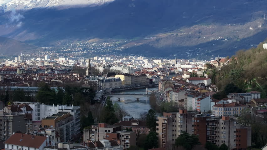 Urban landscape of Grenoble city center featuring the Isere river and its bridges and the French Alps mountains during springtime