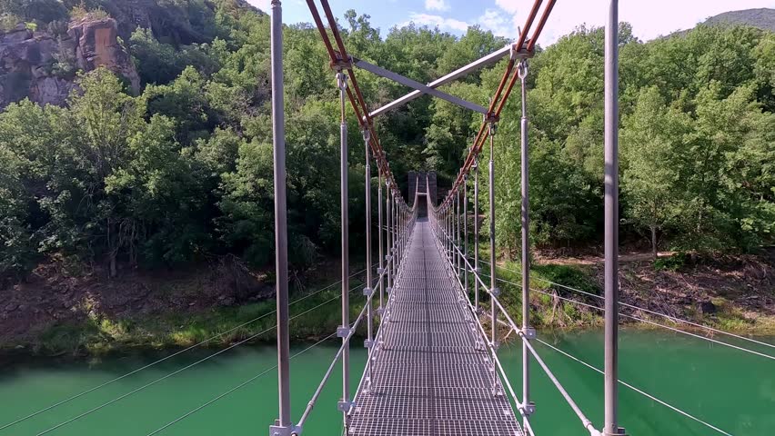 A perspective view of a suspension bridge in Congost de Mont-rebei, Catalonia, showcasing the lush greenery and clear blue skies of the picturesque natural environment.