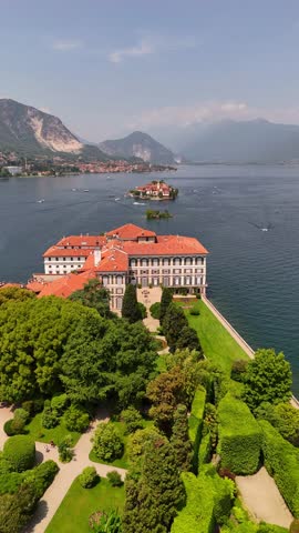 Drone video of Isola Bella’s Borromeo Palace seen from the lake. Elegant red-roofed estate rises above the water, surrounded by Alpine peaks, lush gardens, and sparkling Lake Maggiore, Italy