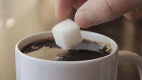 Slow Motion Hand Dropping Sugar Cube Into Black Coffee. Sugar Falling Down Into Coffee Cup. Coffee Caffeine Addiction Junk Food. Concept of Unhealthy Eating, Diabetes, Obesity, Heart Disease.  - Powered by Shutterstock - Get 15% off with code: PIKWIZARD15
