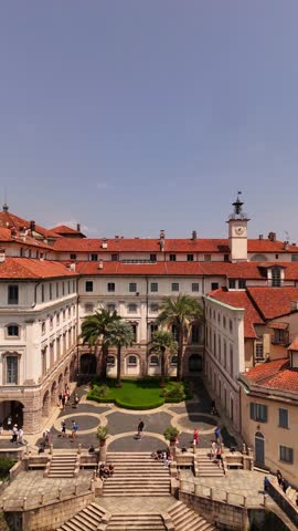 Drone video of Isola Bella’s Borromeo Palace seen from the lake. Elegant red-roofed estate rises above the water, surrounded by Alpine peaks, lush gardens, and sparkling Lake Maggiore, Italy