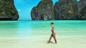 Stylish woman in white bikini strolling slowly along the tropical shoreline of Maya Bay, Phi Phi Islands. Luxury slow motion scene ideal for travel, lifestyle, beauty and summer promotions. - Powered by Shutterstock - Get 15% off with code: PIKWIZARD15