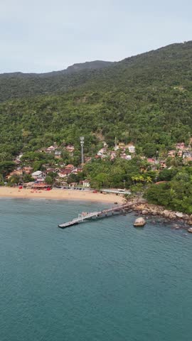 Drone image of a pier at Praia Grande in Ilhabela, surrounded by blue sea, tropical landscape, and coastal vegetation