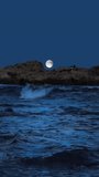 Full moon shines brightly, appearing behind a rugged, dark rocky outcrop. Deep blue ocean waves crash below, creating a powerful and serene nightscape. - Powered by Shutterstock - Get 15% off with code: PIKWIZARD15