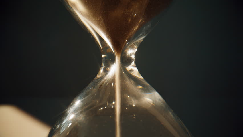 Gold sand grains running inside hourglass measuring passing time in countdown closeup zoom out. Loose particles flowing from one part glass clock to another standing in evening light. Gravity concept.