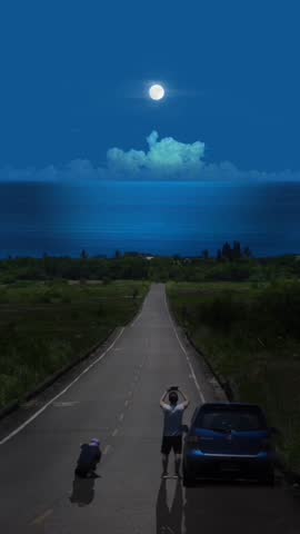 Two people on a quiet road at night, one photographing the full moon over the ocean, car parked nearby. Scenic coastal view, adventure, and capturing memories.