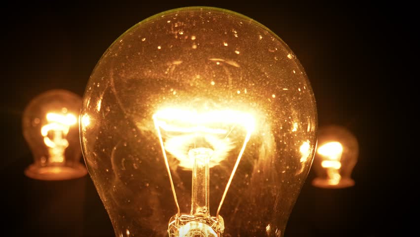 Close up of three glowing incandescent light bulbs against a dark background. One center bulb is extinguished. The warm lighting creates a nostalgic, vintage atmosphere, perfect for energy-related