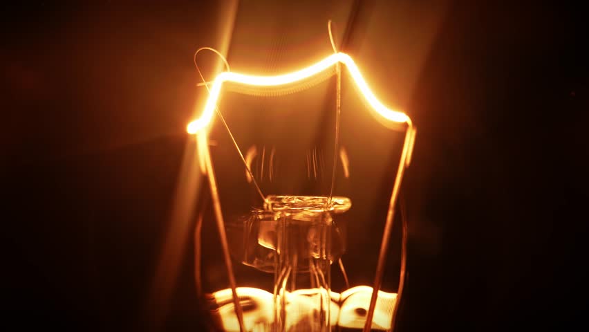 Macro view of a glowing filament in a classic incandescent light bulb. The warm orange lines create a dramatic and minimalistic visual against a black background.