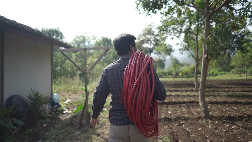 Farmer transporting irrigation hose through cultivated farmland scenery