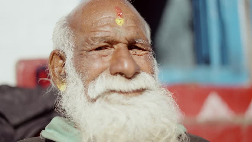 Portrait of senior Indian man with long white beard and intense eyes looking into camera lens, cultural expression, 4k video