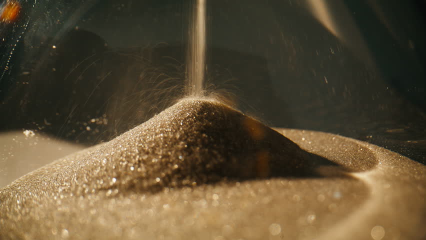 Macro view elegant hourglass in evening light. Closeup gold sand flowing inside transparent glass clock in super slow motion. Vintage timepiece measuring time indoors. Retro device for countdown.