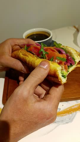 A fresh baguette with salmon, lettuce leaves and a cup of strong coffee. Delicious fish sandwich in your hands