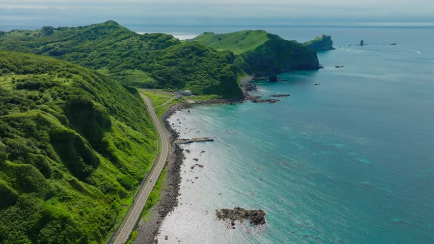Aerial establishing drone fly above car ride in Japanese coastline road at Shakotan beach, Hokkaido, sea cliff landscape