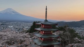 Panoramic view of Mount Fuji at sunset, with a vibrant cherry blossom foreground and a traditional Japanese pagoda. The cityscape of Fujiyoshida stretches between the blossoms and the majestic - Powered by Shutterstock - Get 15% off with code: PIKWIZARD15