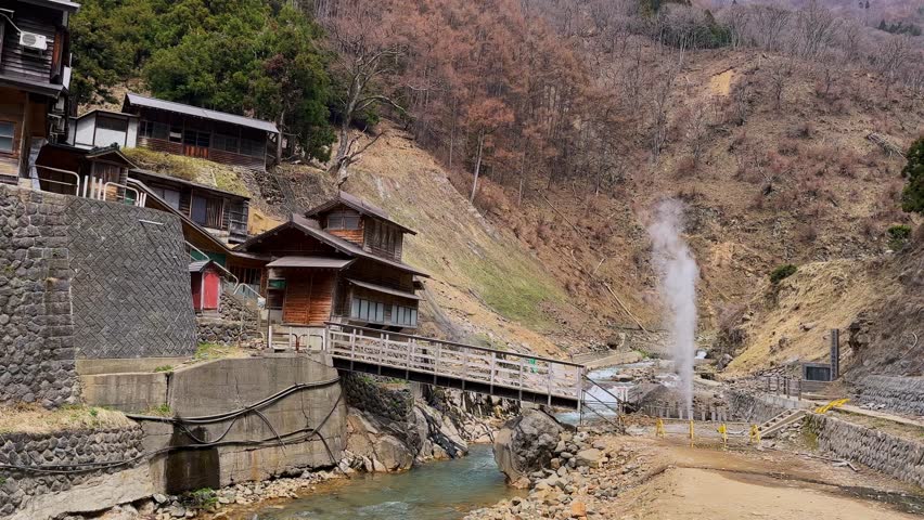 Serene mountain village in Kusatsu, Japan, features traditional wooden houses, a quaint bridge, and a steaming hot spring. Picturesque landscape showcasing rural Japanese architecture and natural