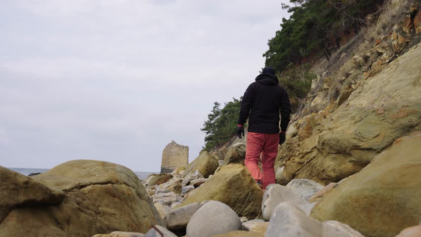 Individual Hiking Up Rocky Slope Towards Coastal Bluff Overlooking Sea