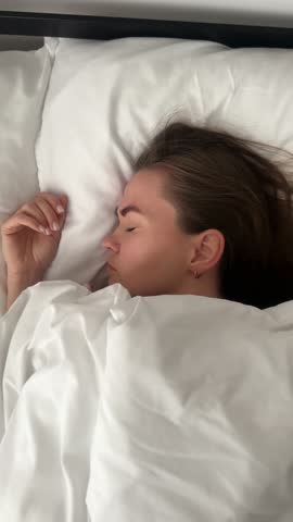 Sleepy young woman face roll over in bed to watch time. Waking up after hard night, stress, insomnia, depression. Mental problems of feeling exhausted, overwhelmed, low energy, burnout.