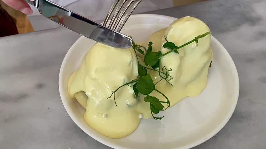 Close-up video of poached eggs being sliced in half, with rich golden yolk flowing out. Perfect for illustrating gourmet breakfast, brunch, or food preparation themes.