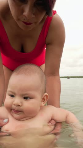 Nurturing mother gently supporting baby boy during first sea swimming experience, showcasing loving bond and careful introduction to water during summer vacation