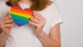 A young woman in a white t-shirt is holding a heart painted with rainbow colors. A strong visual concept symbolizing LGBTQ pride, love, inclusion, and identity. - Powered by Shutterstock - Get 15% off with code: PIKWIZARD15