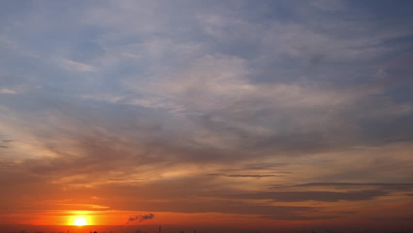 A peaceful sunrise timelapse with warm golden light spreading across the horizon, soft clouds gently moving in the clear blue sky, symbolizing a fresh start and new beginnings. Time lapse.