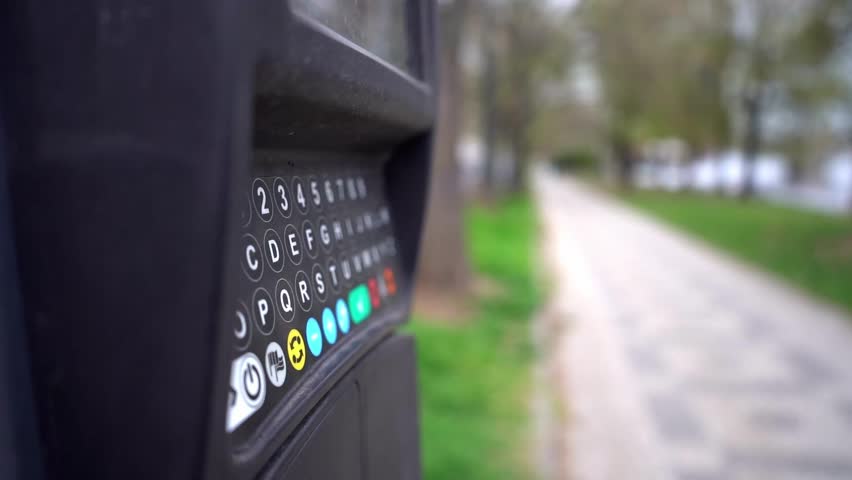 Young woman interacting with a modern parking payment machine, entering information on the touchscreen in an urban outdoor setting, illustrating city parking and self-service technology.

