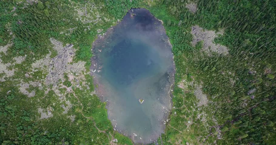 Aerial Top Down View of Mountain Lake Surrounded by Lush Green Forest and Rocks.