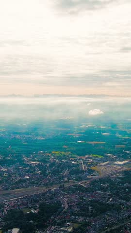 Vertical video. Ghent, Belgium. Sun rays and beautiful clouds. On the ground, a suburb of the city of Ghent with an industrial area and a railway, small houses. Ringvaart in Ghent - water channel, Ae