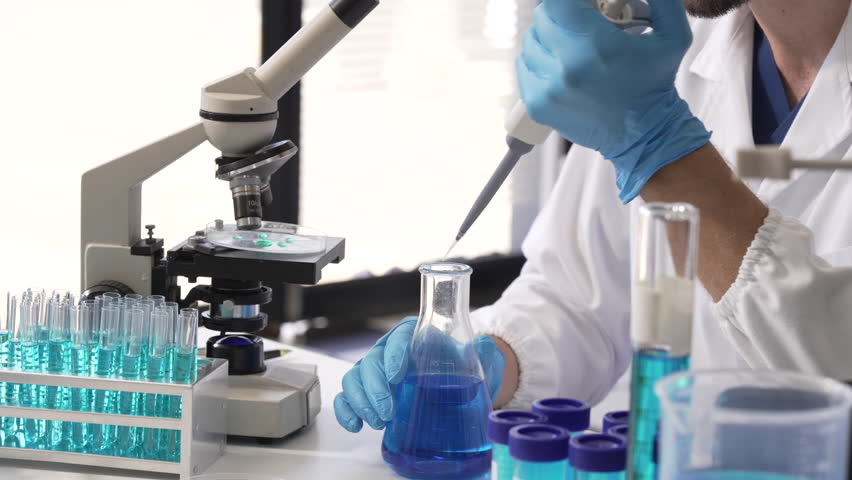 Young Caucasian male scientist works in laboratory, analyzing chemical samples with glassware and microscope. research tools, experiments, data interpretation, pharmaceutical development.