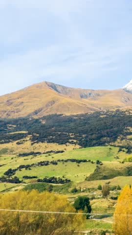A serene mountain landscape with vibrant green hills and golden trees under a clear blue sky