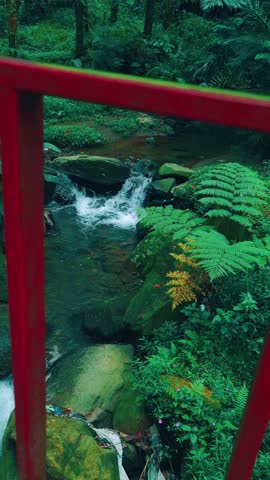 4K UHD footage of a peaceful small waterfall captured from a red bridge, offering a steady long take of serene natural beauty. Shot at 30fps, this tranquil scene is perfect for meditation background