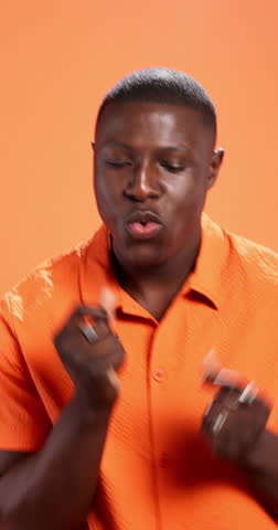Face, dancing and black man in studio, happiness and movement on orange background. African person, excited and model with achievement, energy and celebration with music, winner and confidence