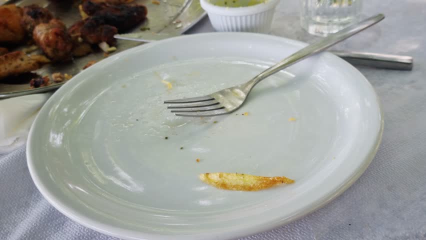 An empty plate with a fork and a single leftover french fry after a meal