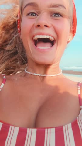 Young woman with long hair smiles brightly while spending time at a beach. She radiates joy and happiness, surrounded by sunny skies and a vibrant atmosphere.
