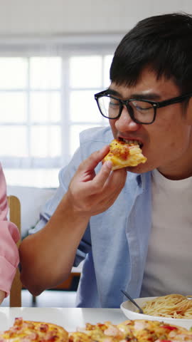 Vertical Screen : Happy young friends group having lunch at home. Asia family party eat pizza food and laugh enjoy meal sitting at dining table together at house. Celebration holiday and togetherness.