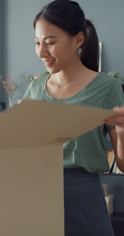 Vertical Screen : Happy Asia lady unboxing cardboard delivery package from online marketplace in living room at house. Satisfied shopper in internet unboxing goods, Online shopping delivery concept.