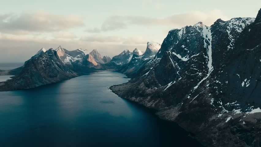 Reine, Lofoten Islands, Nordland, Norway - Steep, Snow-streaked Mountains Rise Dramatically on Either Side of a Calm, Winding Fjord - Aerial Drone Shot