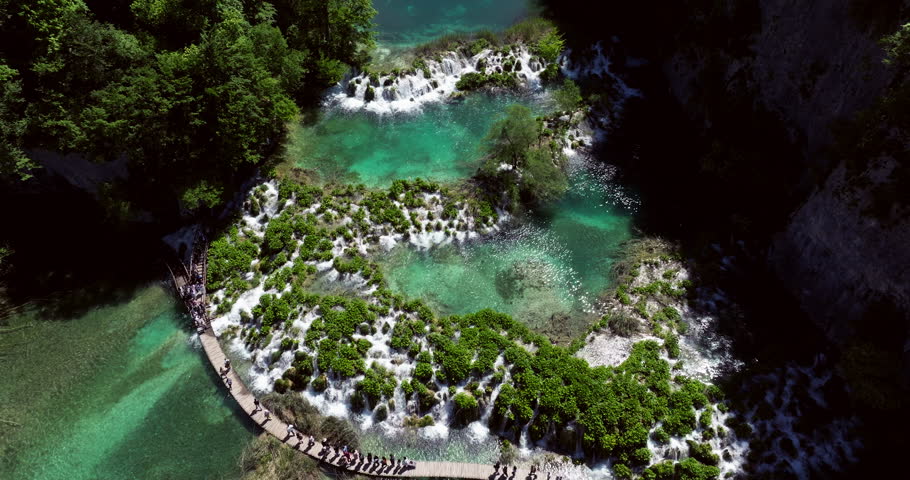 Tourists Walking On Path Through Turquoise Lakes At Plitvice Lakes National Park In Lika-Senj County, Croatia. aerial pullback shot