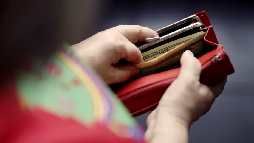 hands holding wallet filled with US dollar bills. Person in colorful clothing handling money, representing personal finance, spending, budgeting, or economic activity. woman counting money in wallet