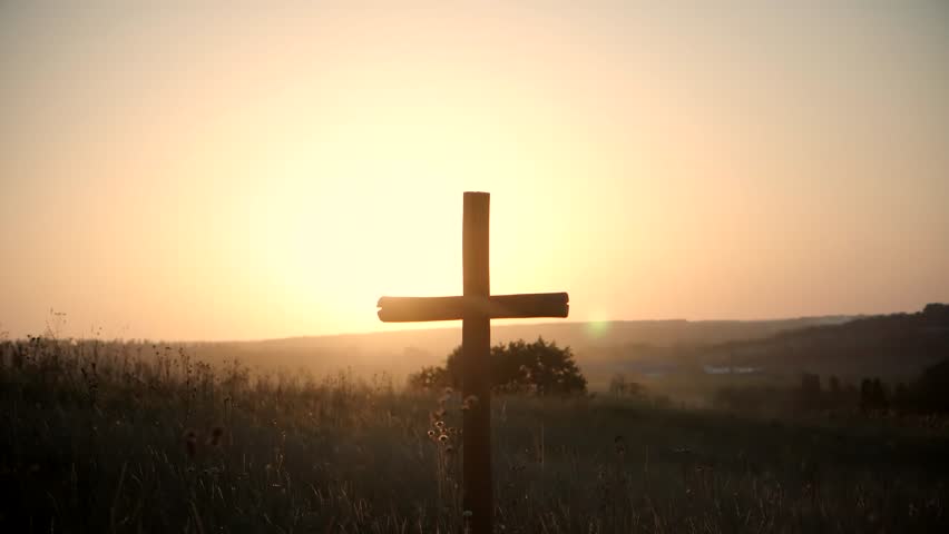 Christian cross. Wooden holy Christian cross stands in grassy field at sunset, silhouetted against warm golden sky. Peaceful rural landscape evokes faith, spirituality, hope and remembrance religion 