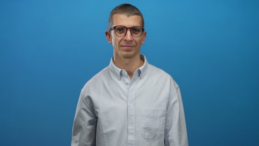 Caucasian man in glasses makes triumphant gesture against isolated blue wall background, wearing a striped shirt, conveying confidence and achievement. - Powered by Shutterstock - Get 15% off with code: PIKWIZARD15