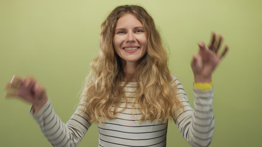 Woman framing eyes with hands while peeking in studio as blonde young performer gives a smile and tongue expression against a green striped backdrop.